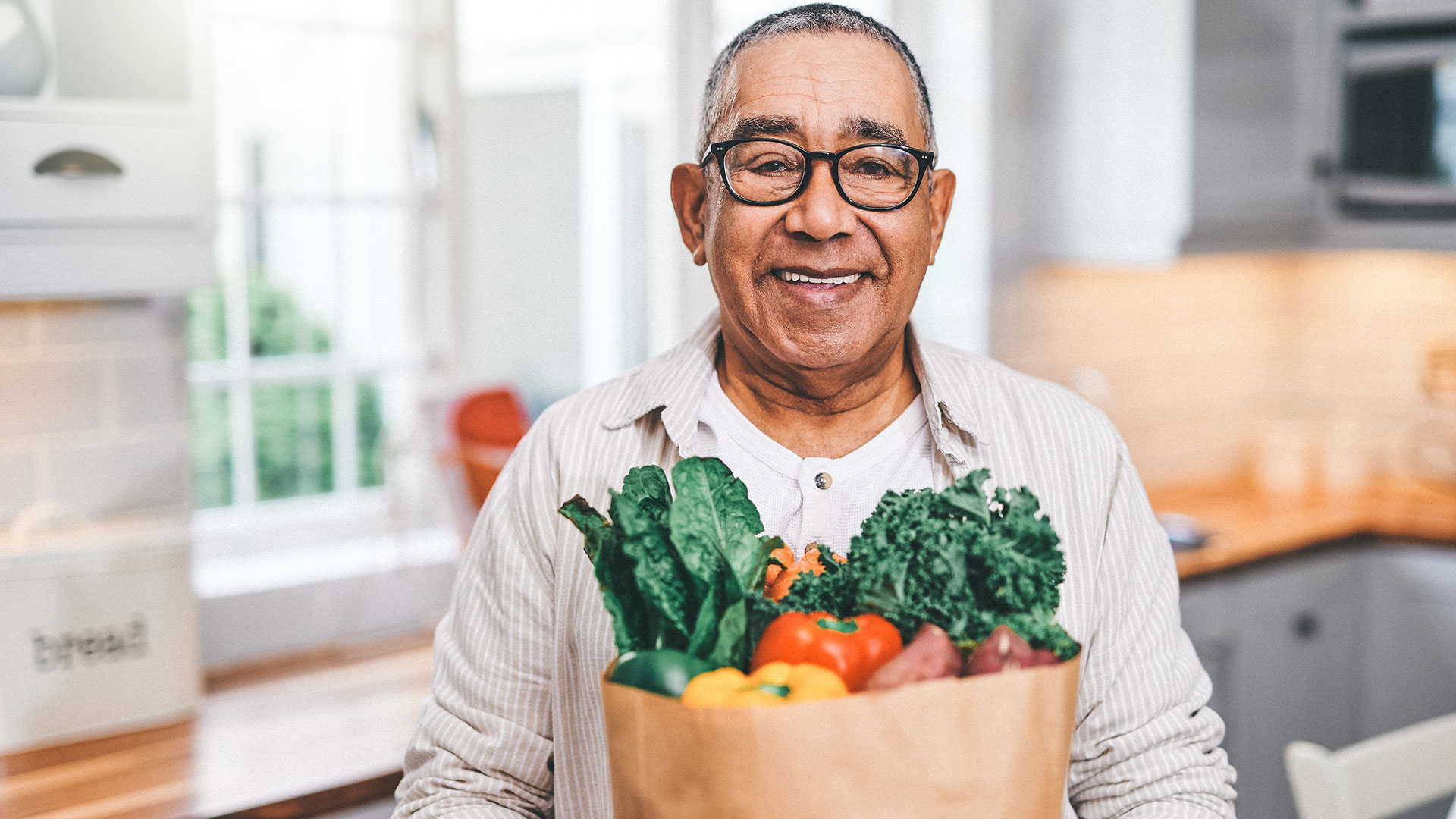 older man holding bag full of vegetable groceries